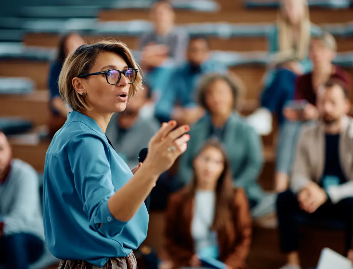 A woman passionately teaching a diverse classroom audience.