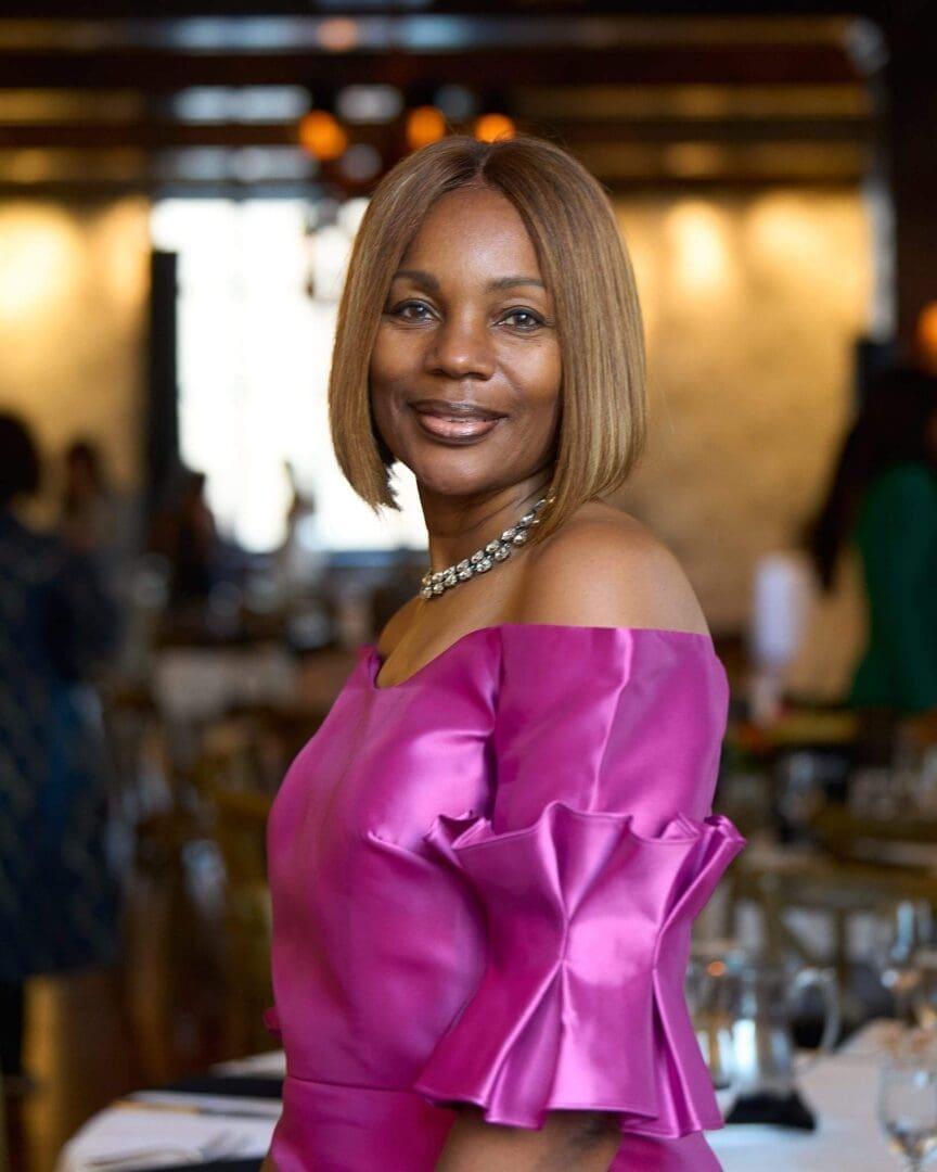 Woman in a vibrant pink satin dress smiling warmly indoors.