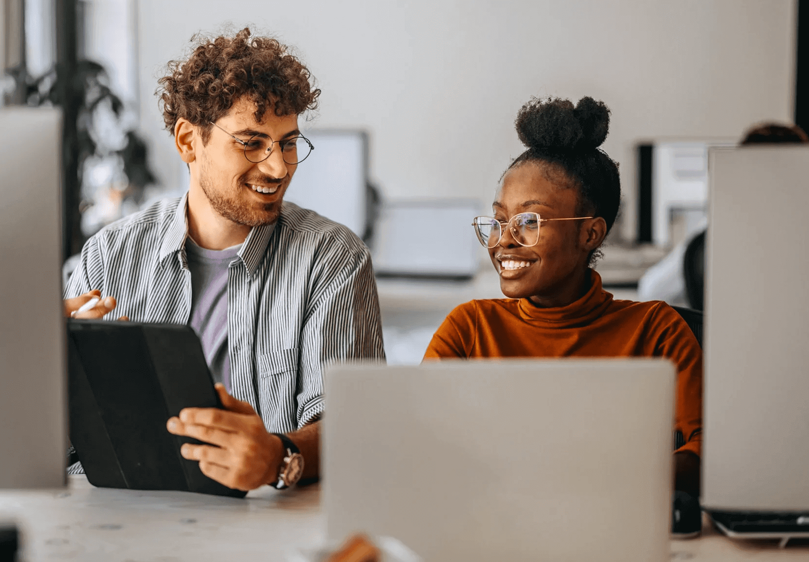 Two colleagues sharing ideas while working on laptops in a bright office